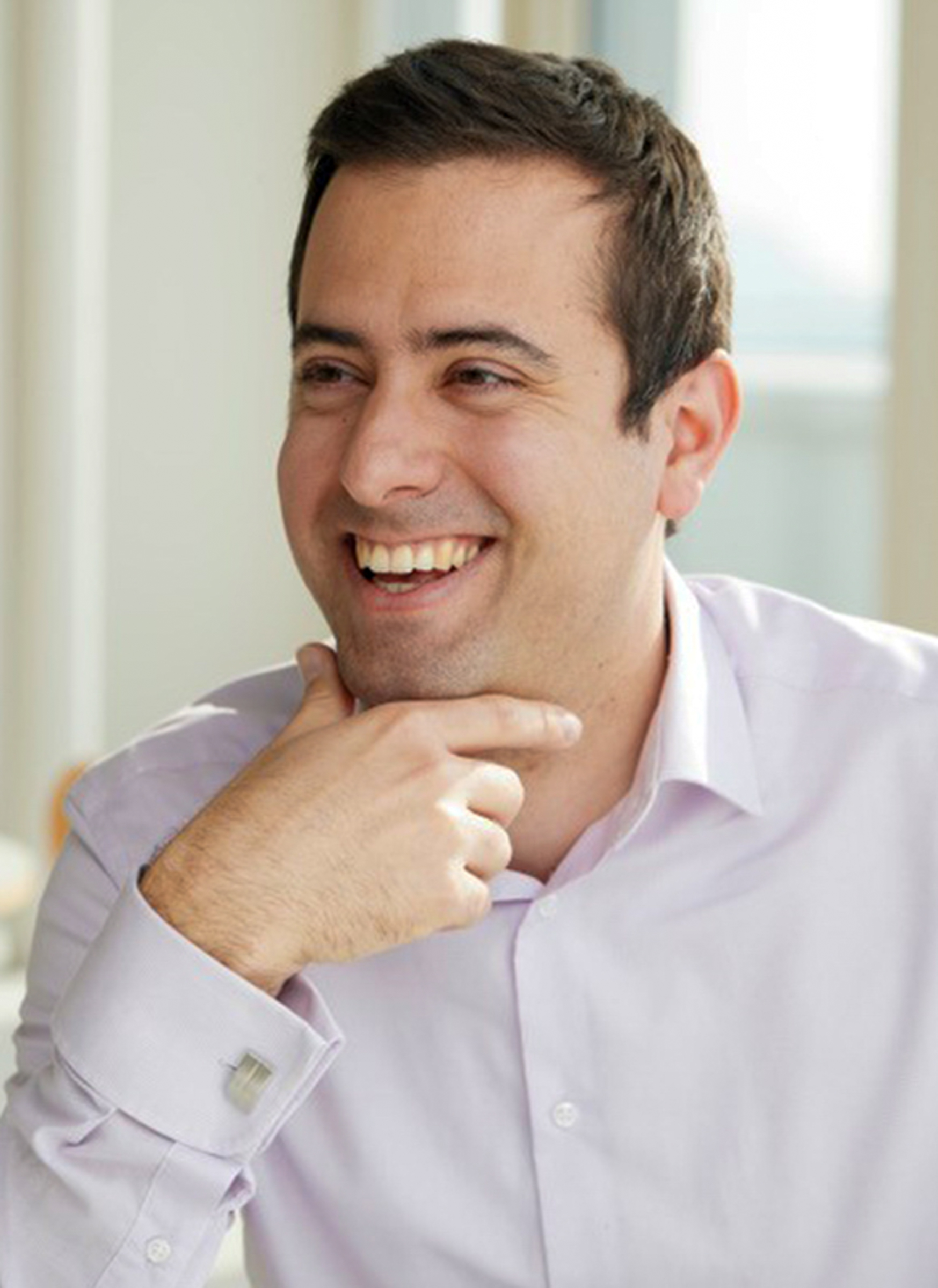 A professional headshot of a man, Bence Gyorgy. He has a hand on his chin and he is looking off to the side with a wide smile. He has short brown hair.