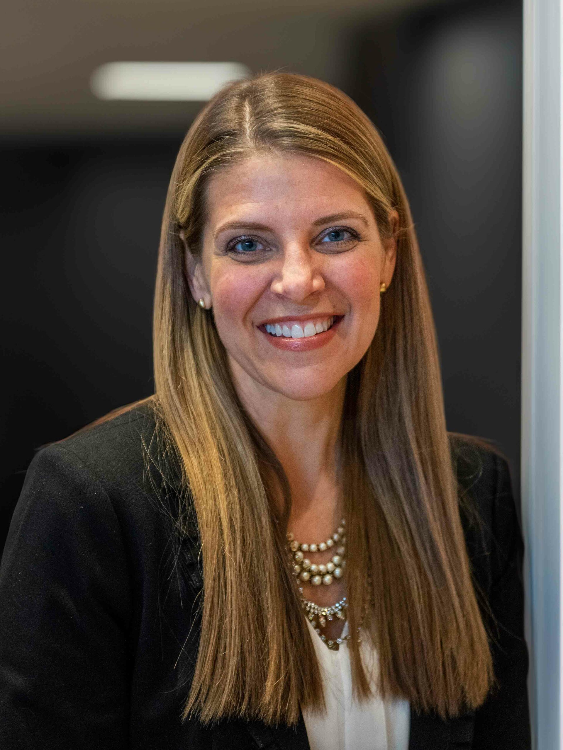 A professional headshot of a woman, Peggy Borst. She has straight light brown hair and she wears a suit jacket. She is smiling and looking directly ahead.