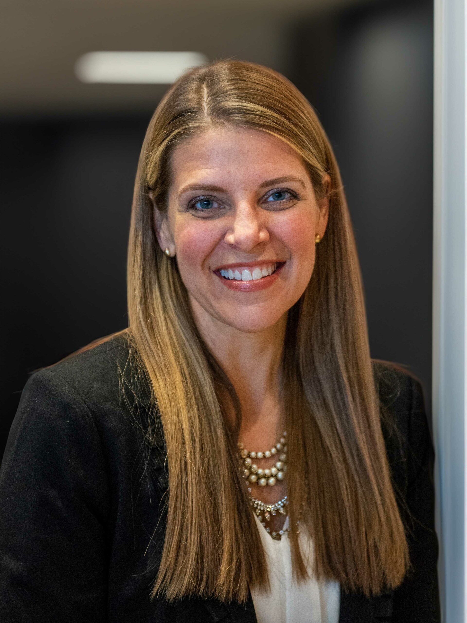 A professional headshot of a woman, Peggy Borst. She has straight light brown hair and she wears a suit jacket. She is smiling and looking directly ahead.