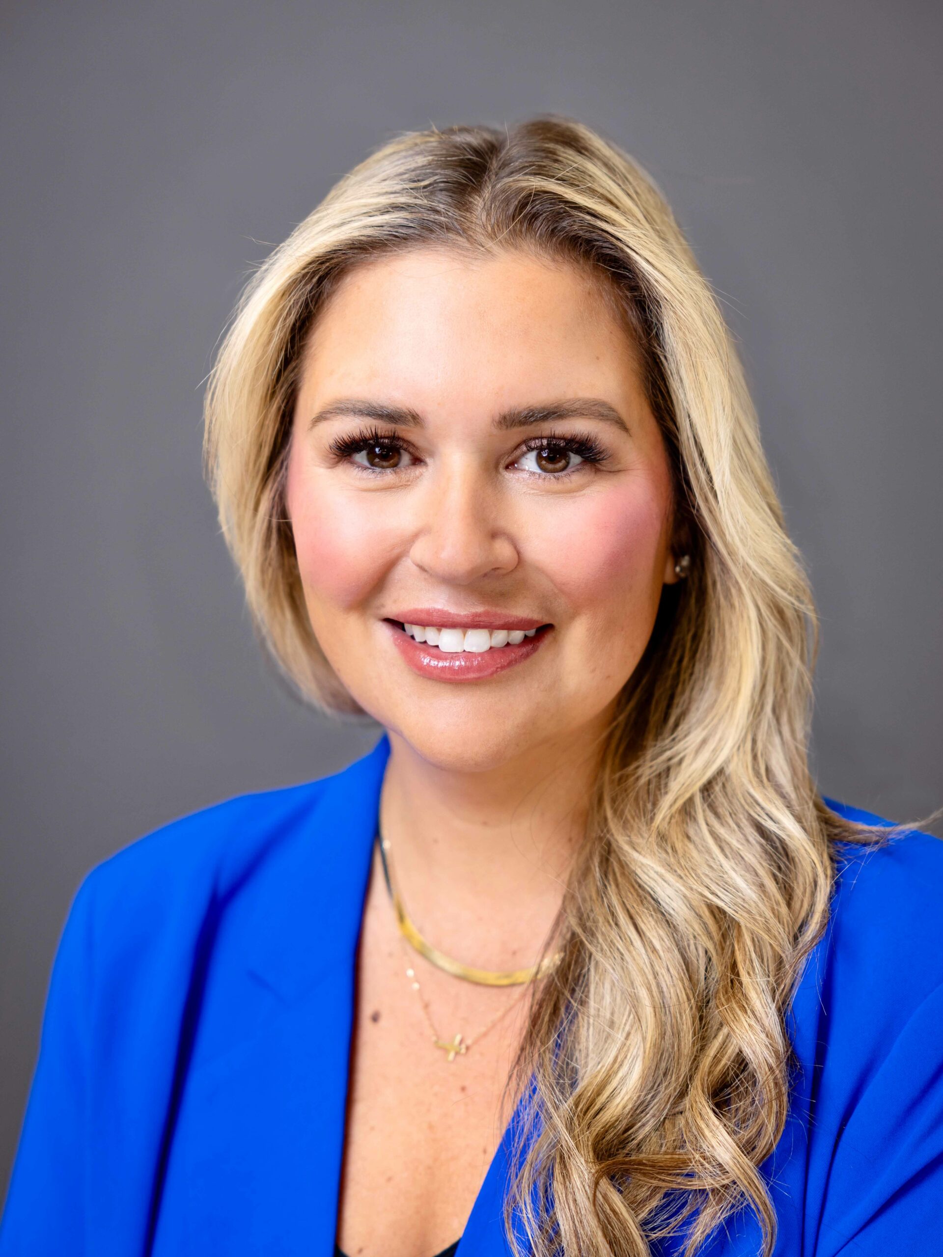 A professional headshot of a woman, Tori Banu. She has blonde hair and she wears a bright blue blazer. She is smiling and looking straight ahead.