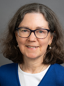 Headshot of Marly Kenna. She has shoulder length brown hair and wears glasses. She is wearing a white shirt with a blue cardigan and she is smiling.