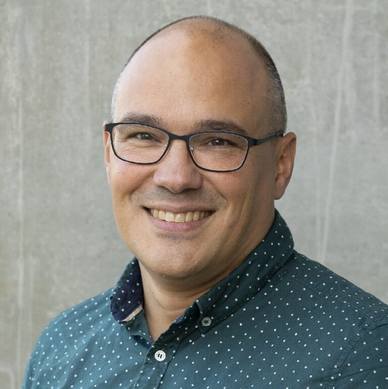 a man wearing glasses and a collared shirt smiling