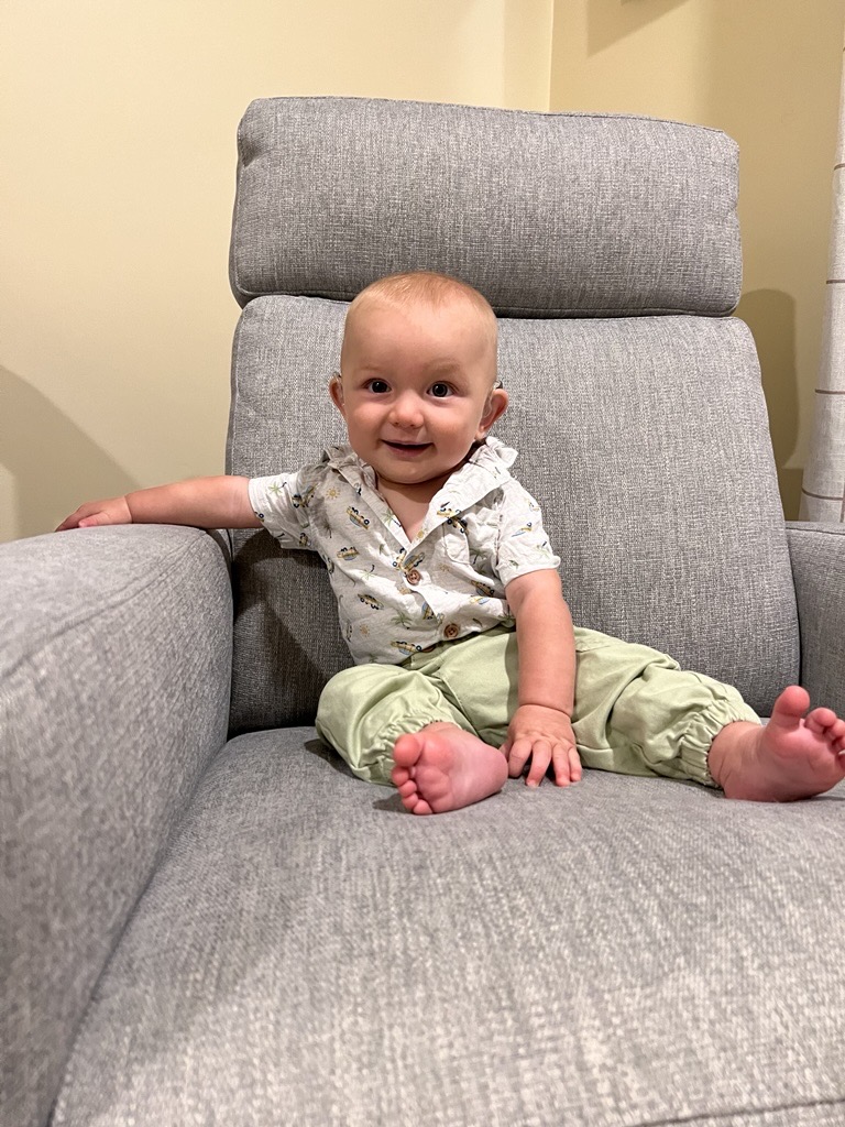 Joey sits on a grey couch with a big smile on his face