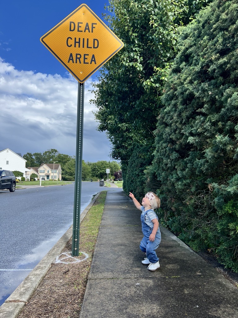 Joey Deaf Child Area Joey Stands outside pointing at a traffic sign that says "Deaf Child Area"