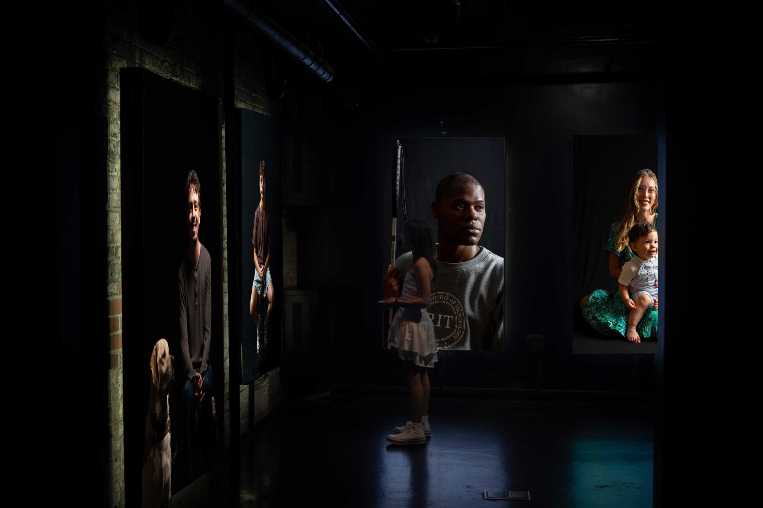 An image of a girl standing in a dark room surrounded by portraits taken by the Usher Syndrome Society