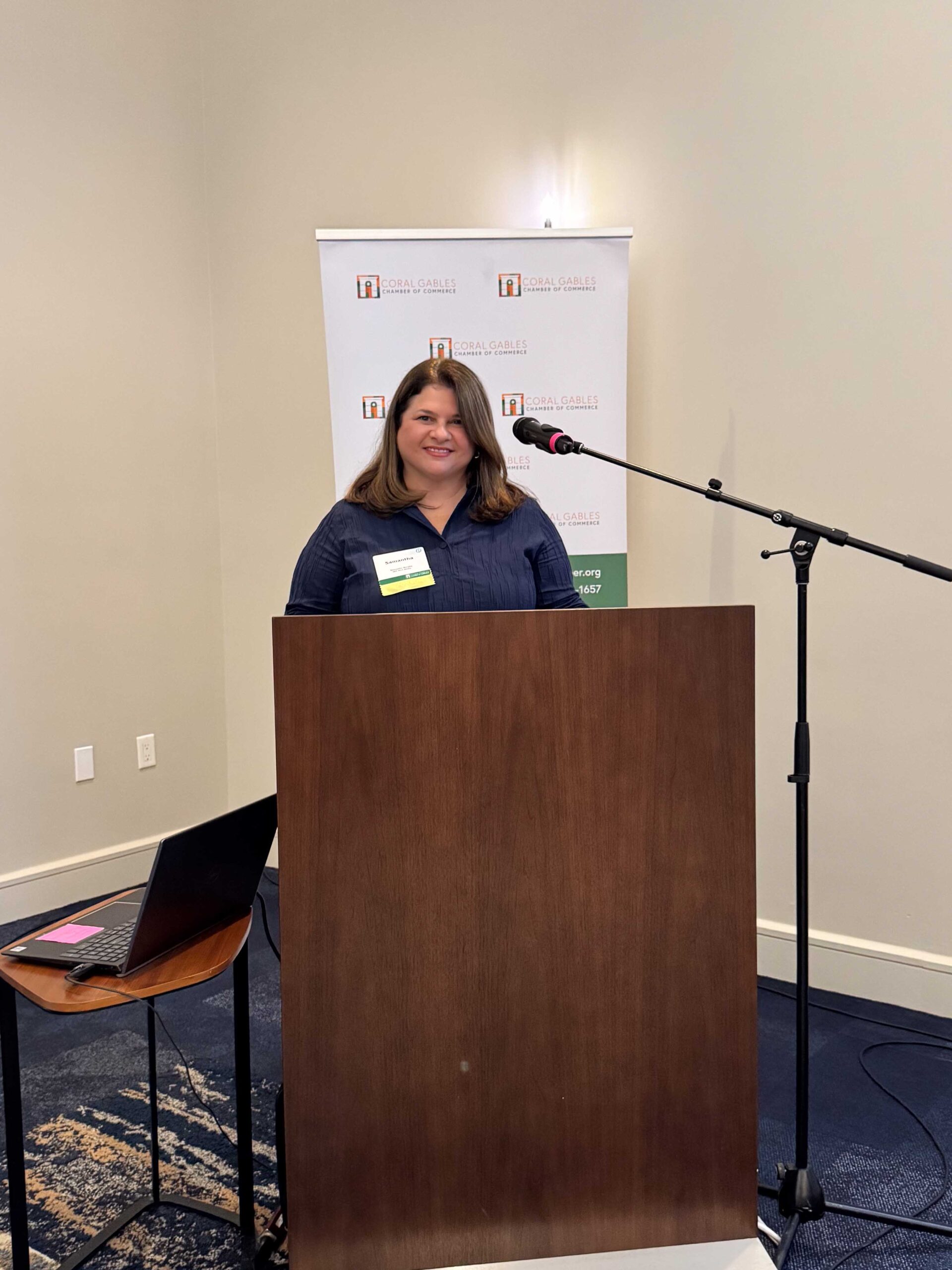 Samantha stands at a podium speaking during a Coral Gables Chamber of Commerce event