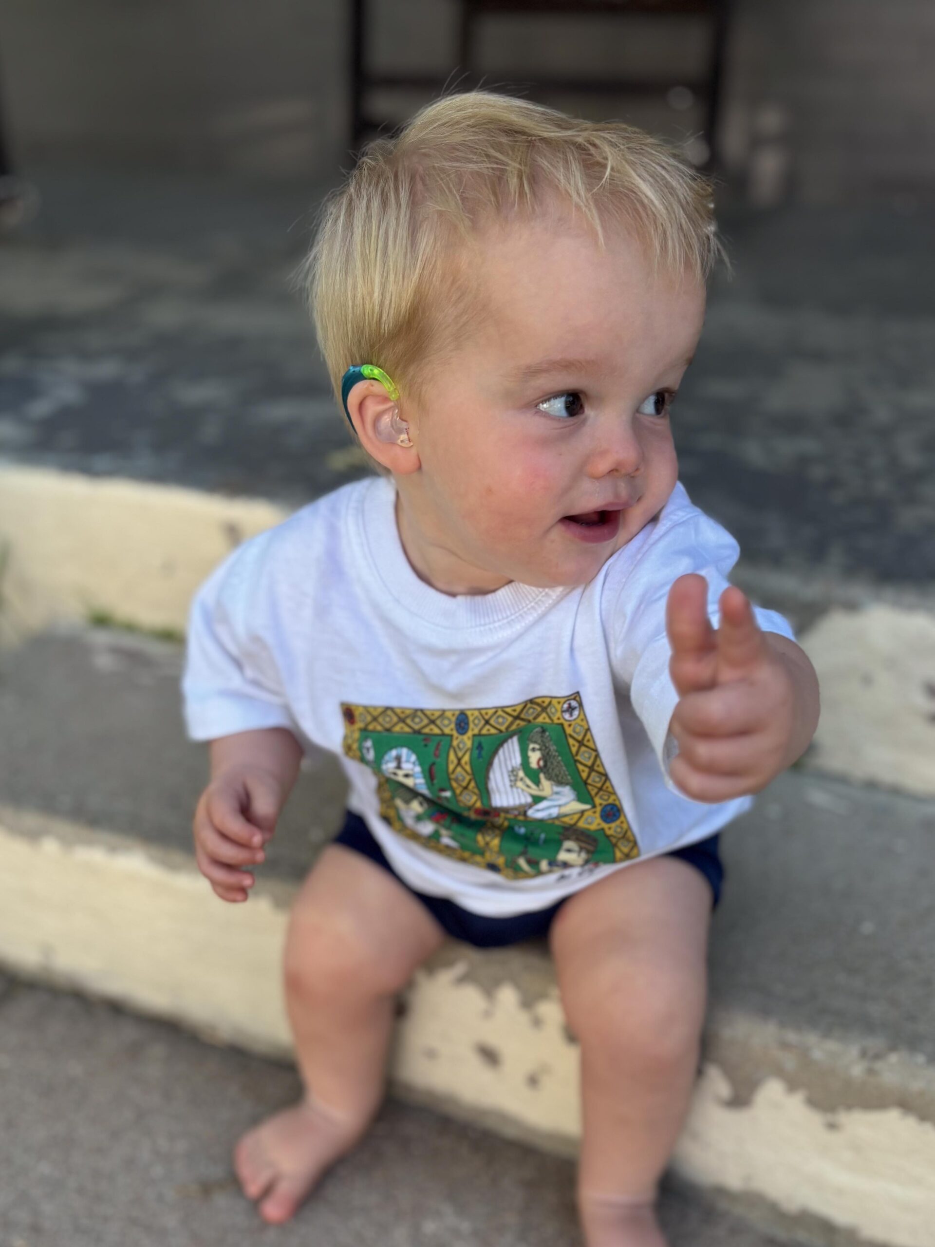 Joey is outside wearing a big hat and swinging on a swingset