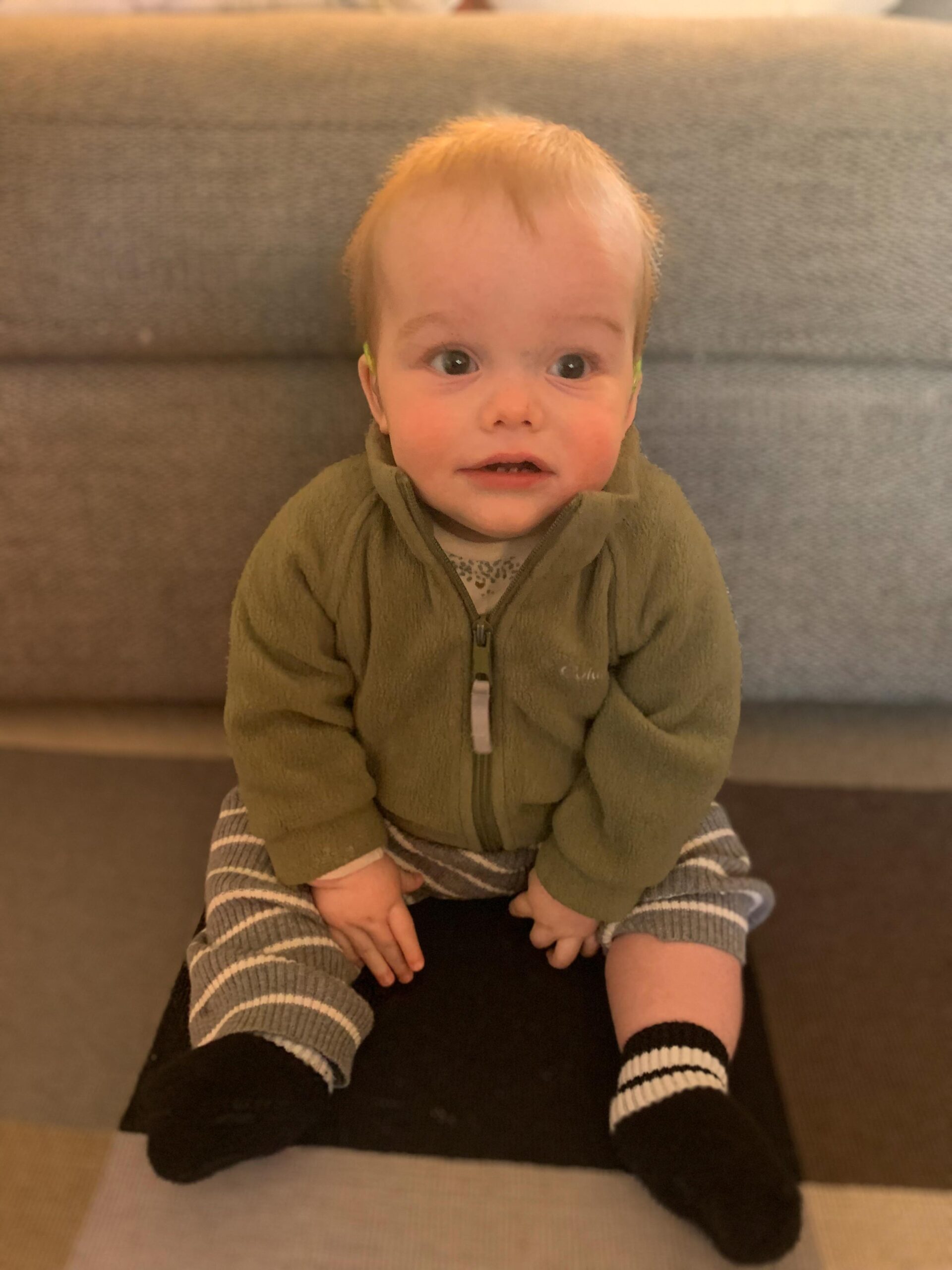 Joey sits on a grey couch with a big smile on his face