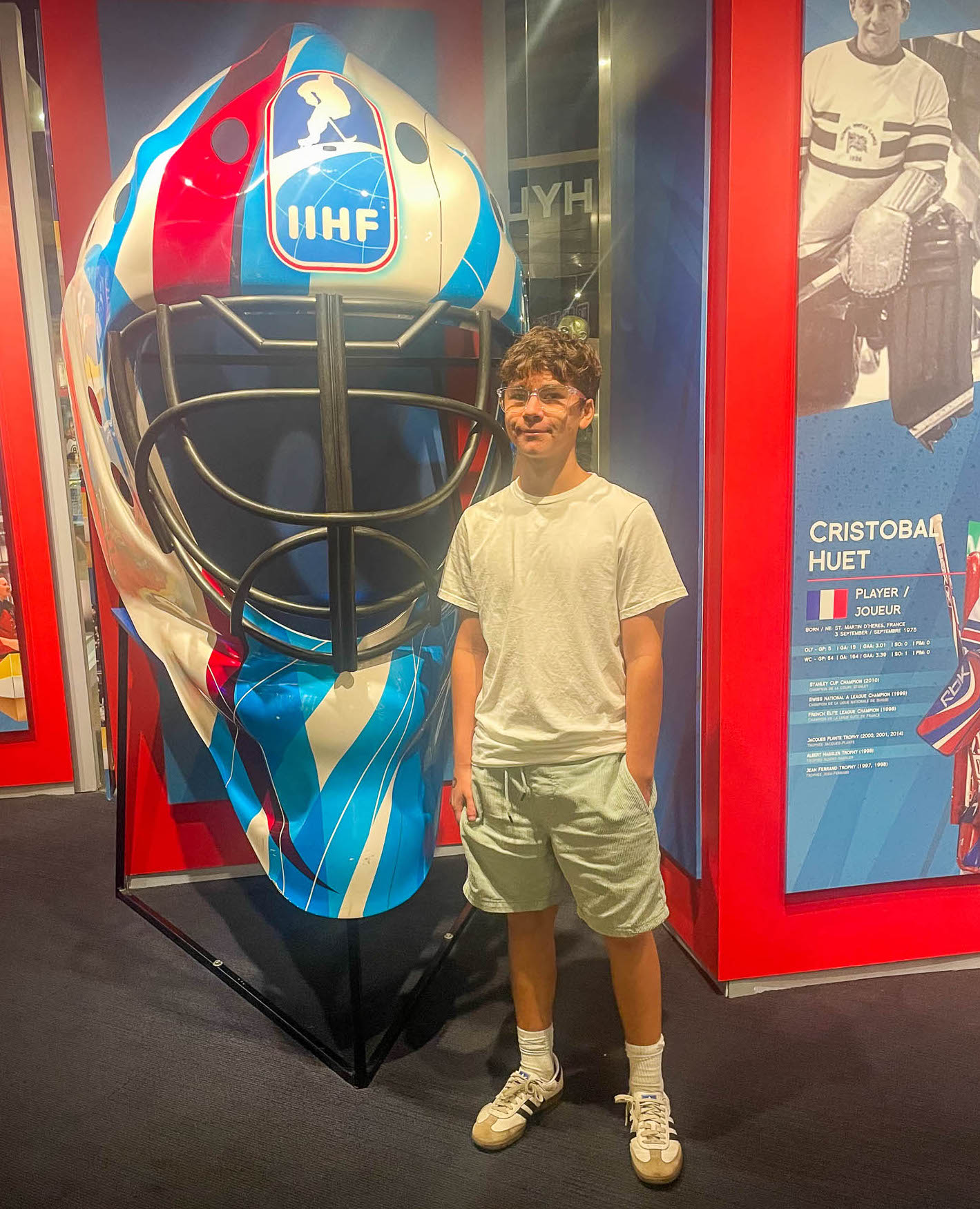Americo at the NHL Hall of Fame standing in front of a giant hockey mask with  the IIHF logo on it.