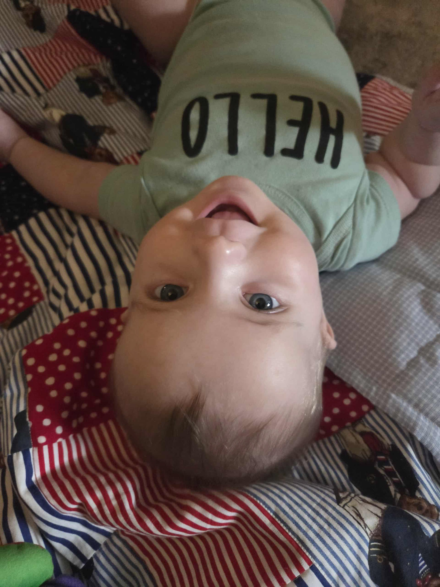 Norik as a small baby looking up at the camera wearing a green shirt that says "Hello"