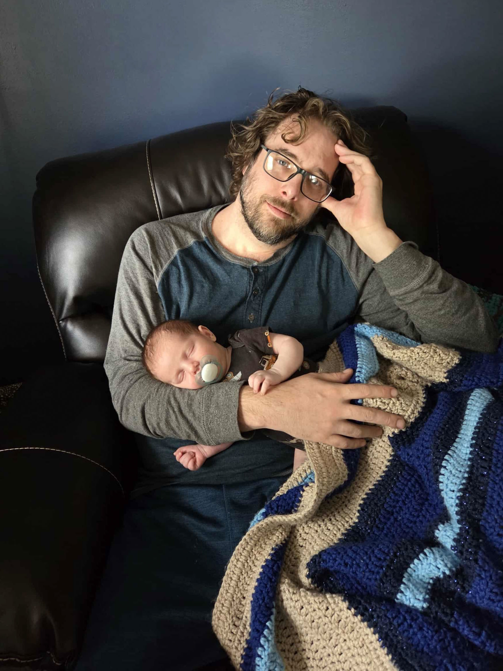 Joey sits on a grey couch with a big smile on his face