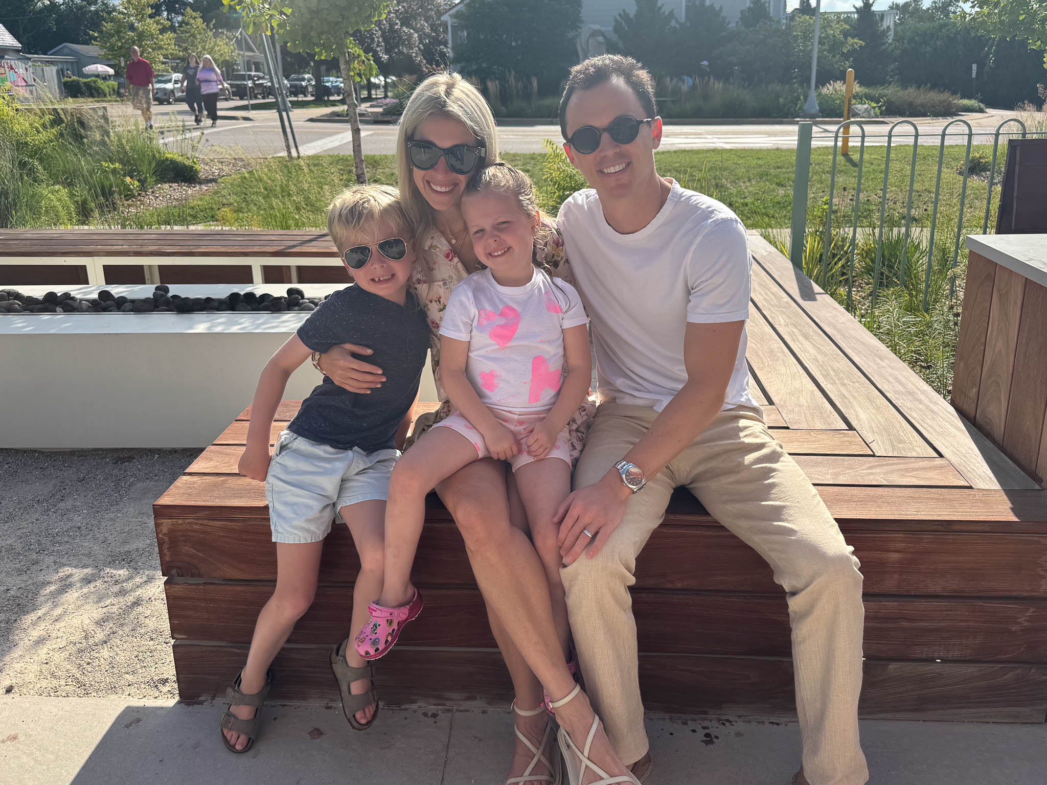 Jon Schultz with his wife and two children sit outside together on a modern bench.