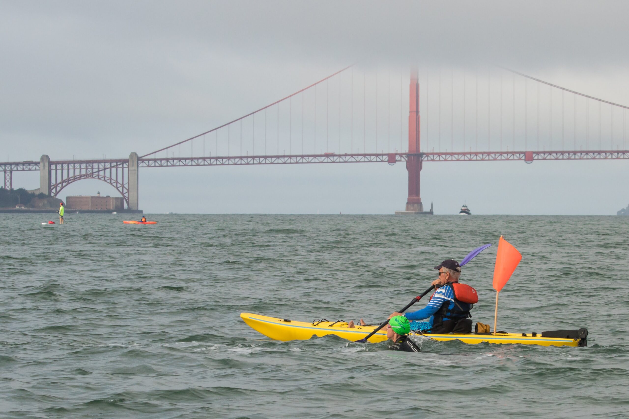 A kayaker paddles in the San Francisco Bay next to a swimmer. The Golden Gate bridge is in the background