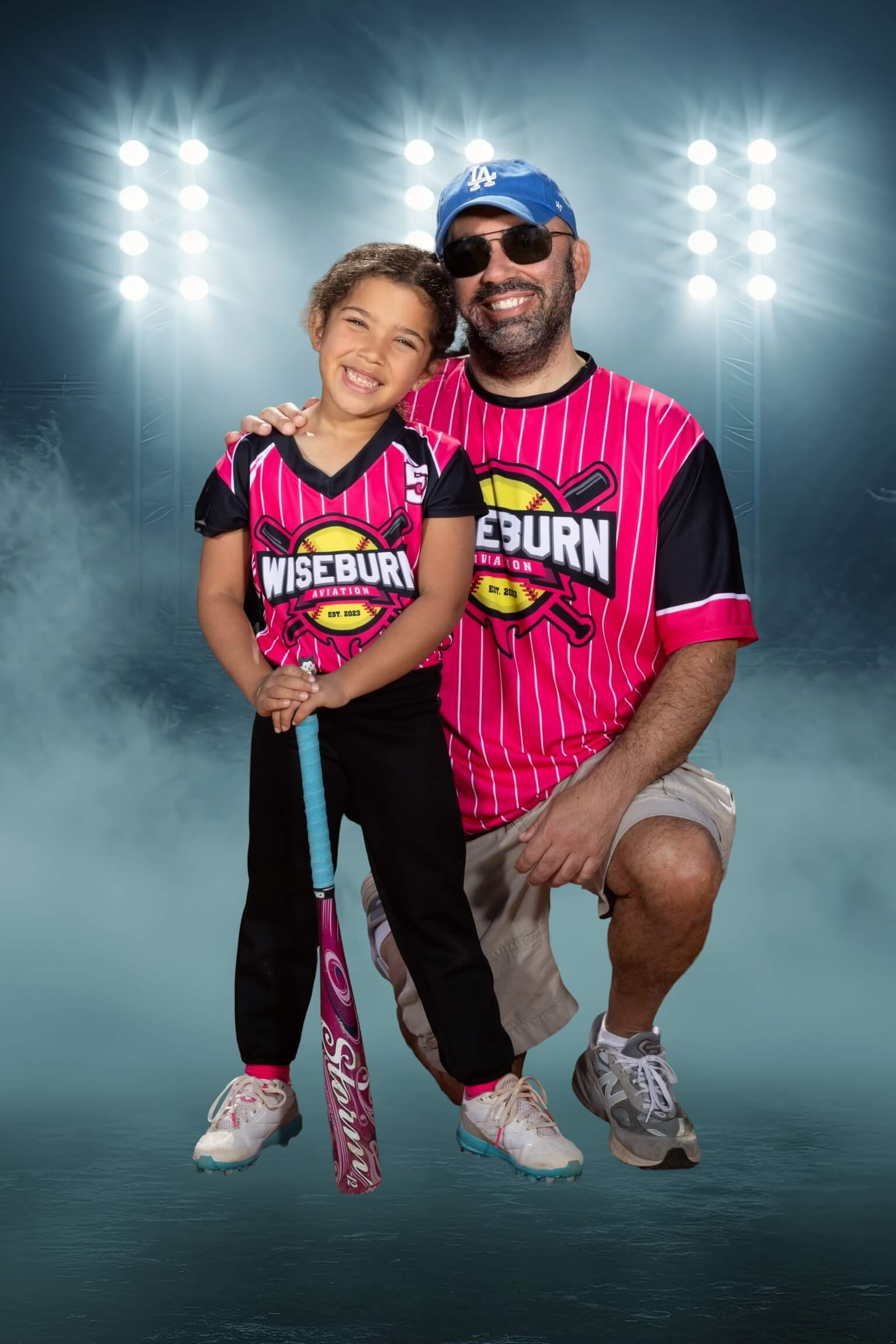 Brendan and his daughter both wearing pink sports jerseys. His daughter holds a baseball bat.