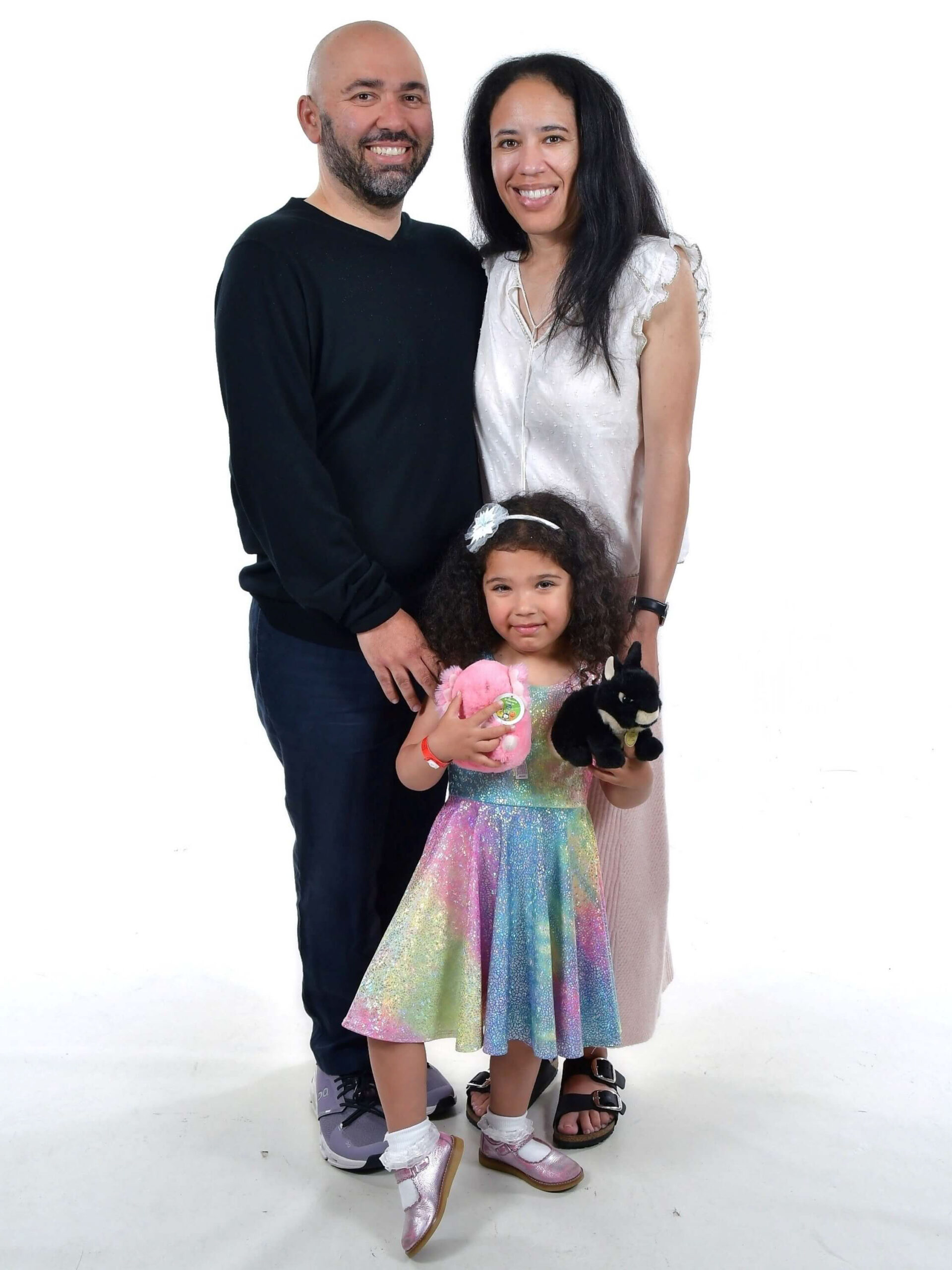 Brendan, his wife Candace, and their daugher smile for a family photo in front of a white background.