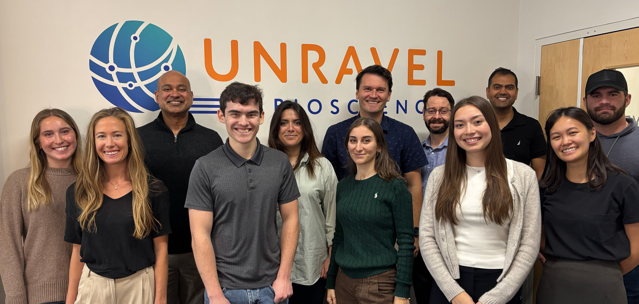 A group photo of the team at Unravel Biosciences. They stand in front of their company logo.