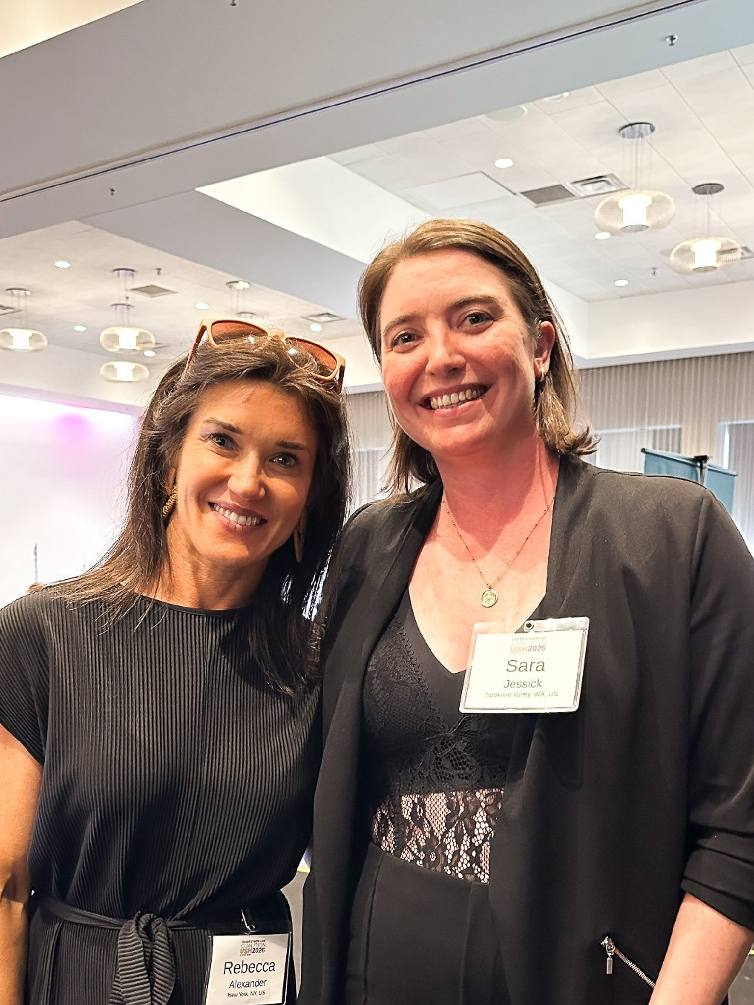 Two women pose for a photo together at the Usher syndrome conference. They are both smiling and looking at the camera. One of the women is Sara Jessick and the Other is Rebecca Alexander