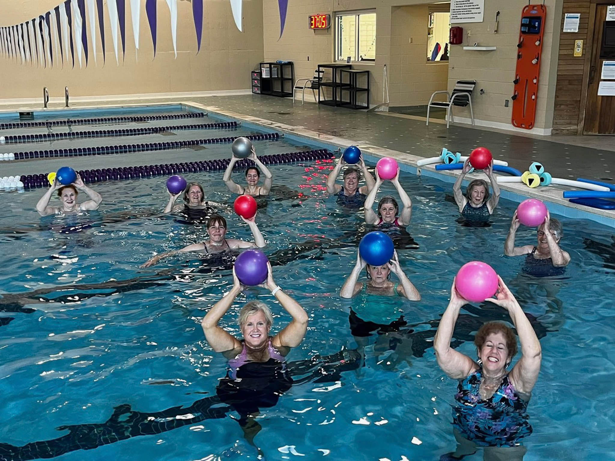 A group of people in an indoor swimming pool doing water aerobics holding a ball above their heads