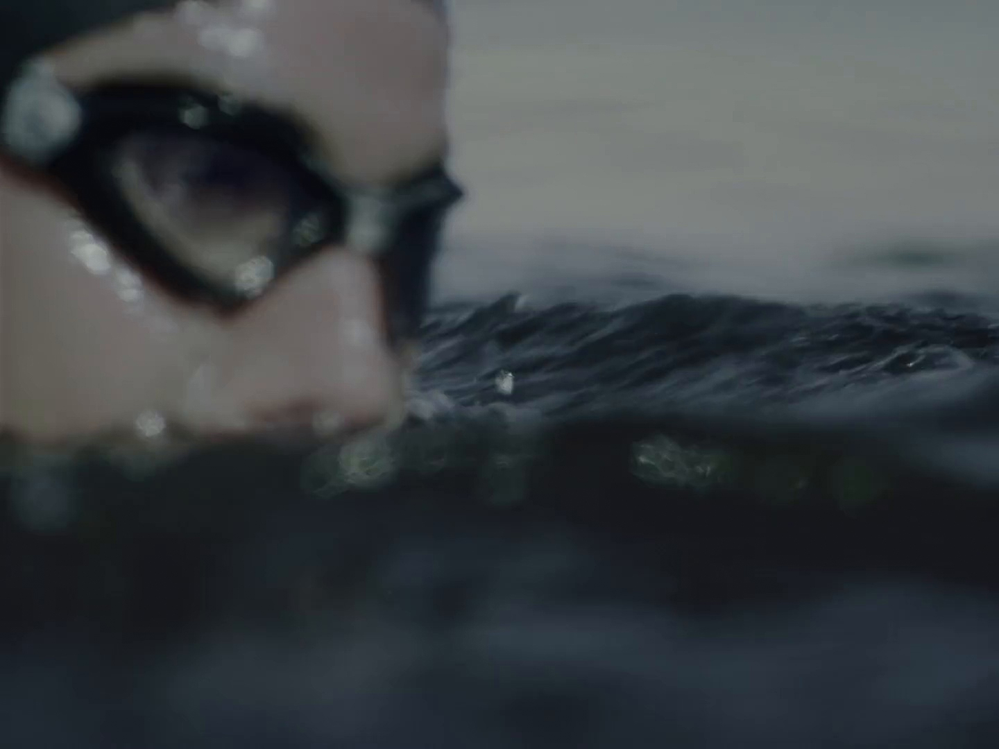 A close up image of a person wearing goggles in the water swimming. 